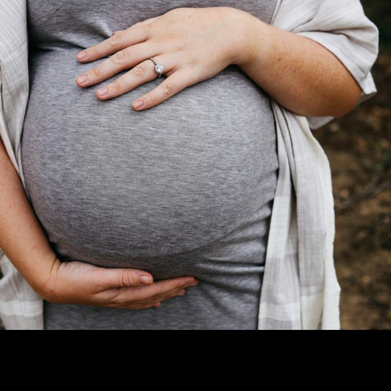 Lymphdrainage Physiotherapie Lutherstadt Wittenberg Schwangere Frau hält ihren Bauch, trägt ein graues Kleid und eine leichte Jacke.