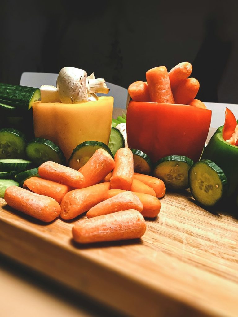 Gemüseschalen mit Karotten, Paprika und Gurken auf einem Holzbrett.