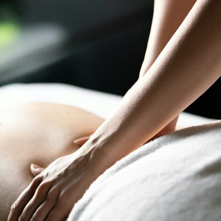 Frau gibt eine Massage an einer liegenden Person in einem ruhigen Wellnessraum.