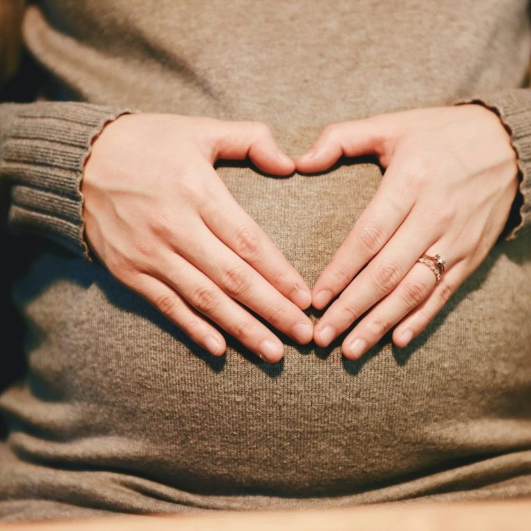 Physiotherapie Schwangerschaft Hände formen ein Herz über einem schwangeren Bauch.